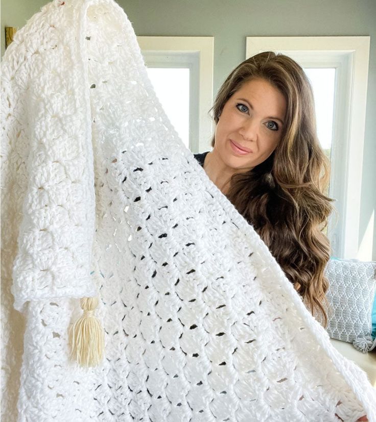 a woman holding up a white crocheted blanket