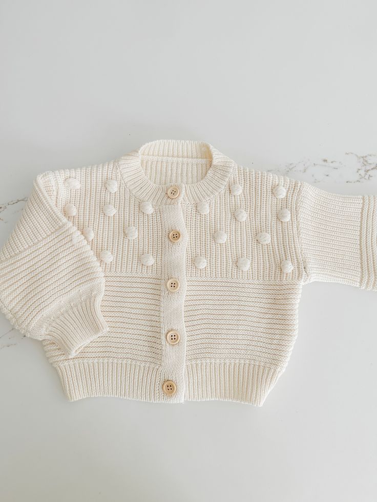 Soft and cozy, this stunning knit cardigan is the perfect addition to your little ones closet. Tiny Pom Pom appliqués all over. Textured pattern with front buttons. Playful Knit Long Sleeve Outerwear, Playful Cotton Knitted Cardigan, Playful Knitted Cotton Cardigan, Cute Cream Soft Knit Sweater, Playful Long Sleeve Knit Cardigan, Soft Knit Long Sleeve Sweater For Playtime, Cute Cotton Cardigan With Button Closure, Cute Cotton Buttoned Sweater, Cute Cotton Sweater With Buttons