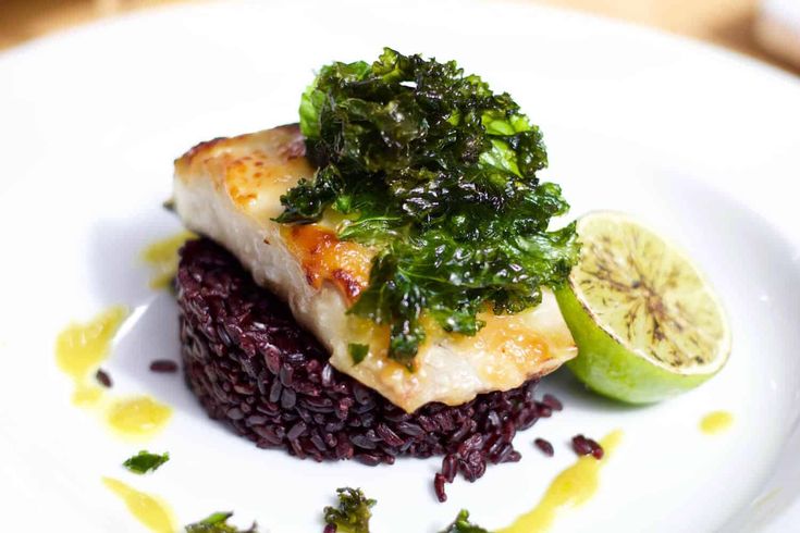 a white plate topped with fish and rice covered in sauce next to a slice of kiwi