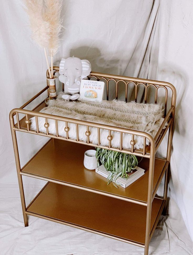 a gold metal baby crib next to a shelf with items on it and a white background