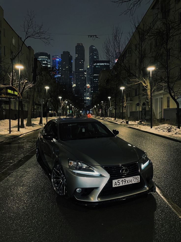 a silver car parked on the side of a road at night with city lights in the background