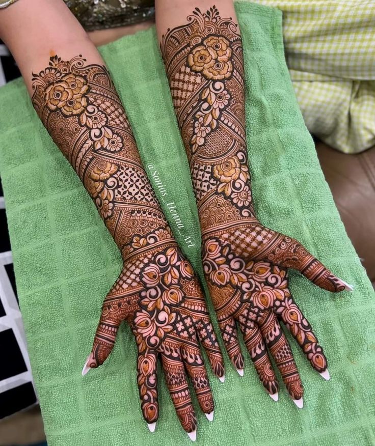 two hands with henna tattoos on them sitting on a green towel next to each other