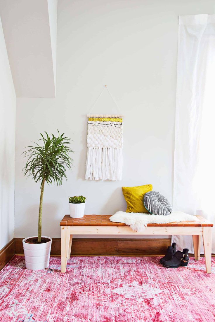 a room with a pink rug, white walls and a wooden bench in front of a potted plant