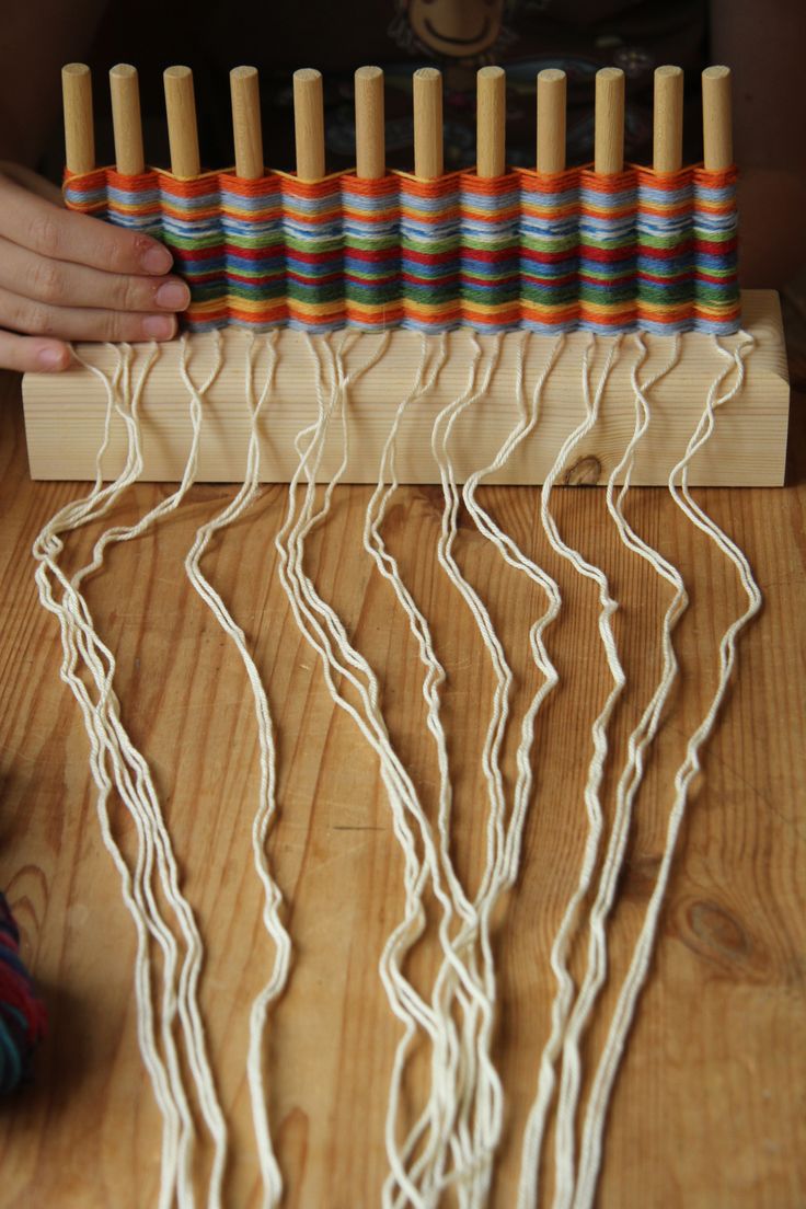 a person is weaving white yarn on a loom with several skewers in the background