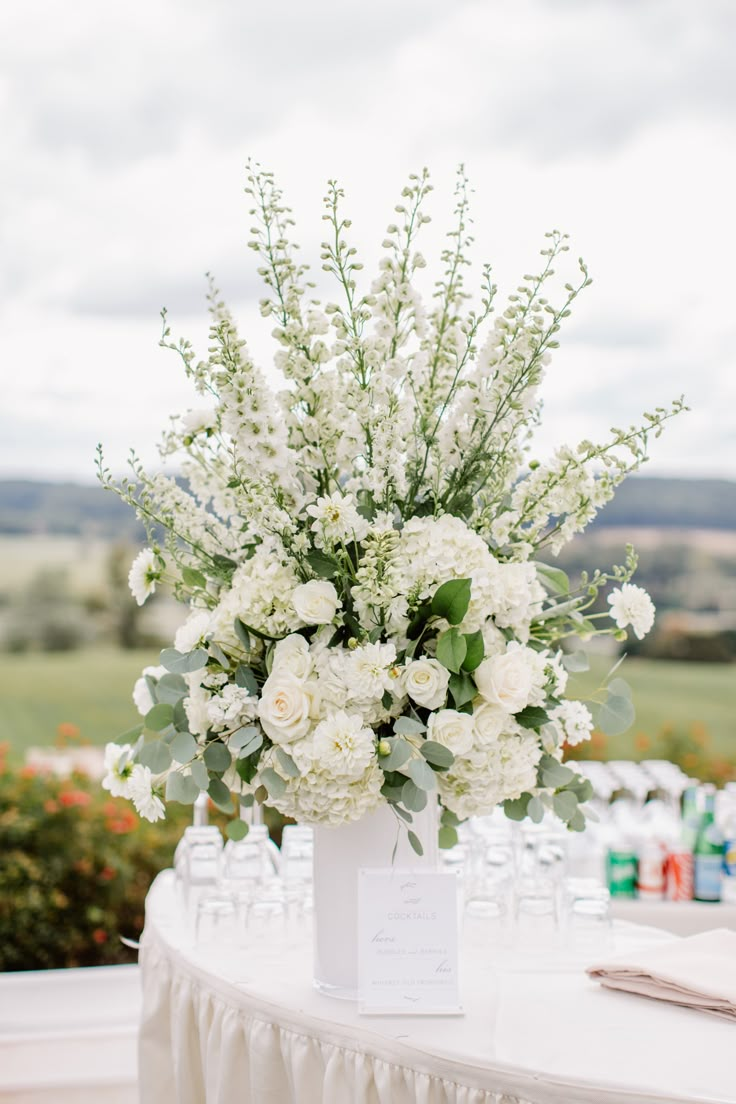 a vase with white flowers and greenery is on a table at a wedding reception