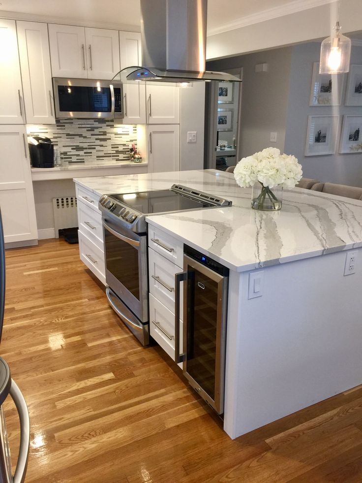 a kitchen with white cabinets and marble counter tops, stainless steel appliances and an island