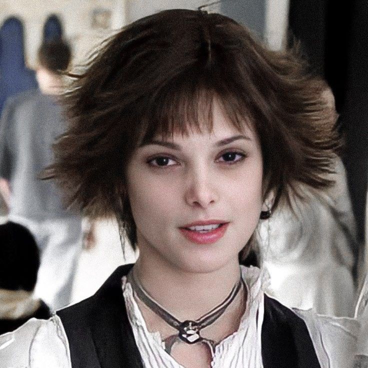 a woman with short hair wearing a white shirt and black vest is looking at the camera