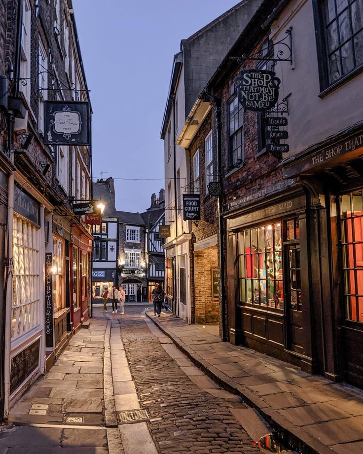 an empty street with people walking on the sidewalk and buildings in the background at dusk