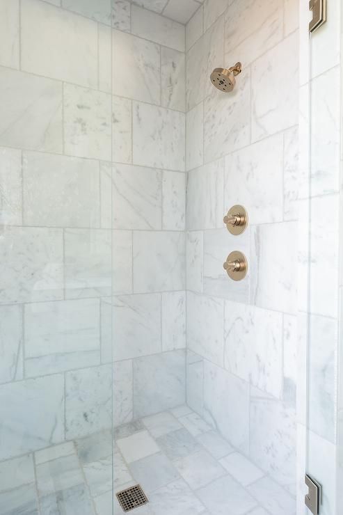 a walk in shower sitting next to a white tiled wall with gold faucets