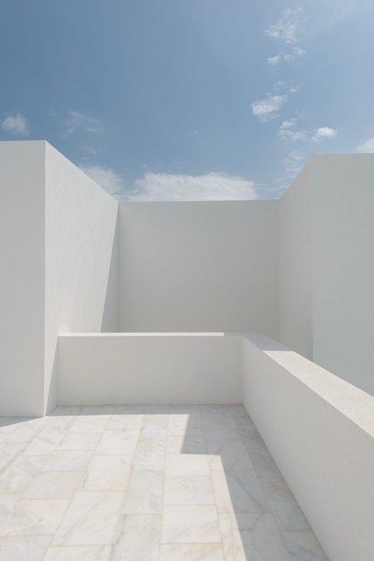 an empty room with white walls and tile flooring, under a blue cloudy sky