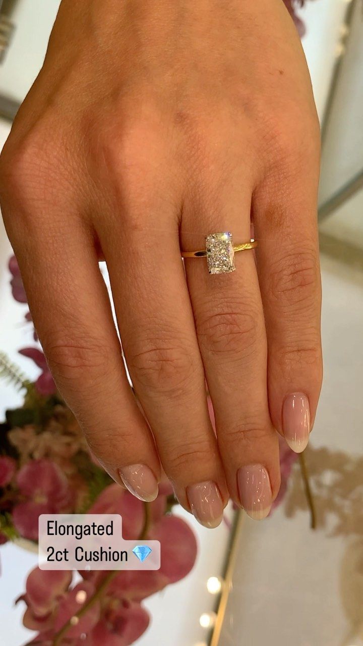 a woman's hand with a diamond ring on top of her finger and flowers in the background