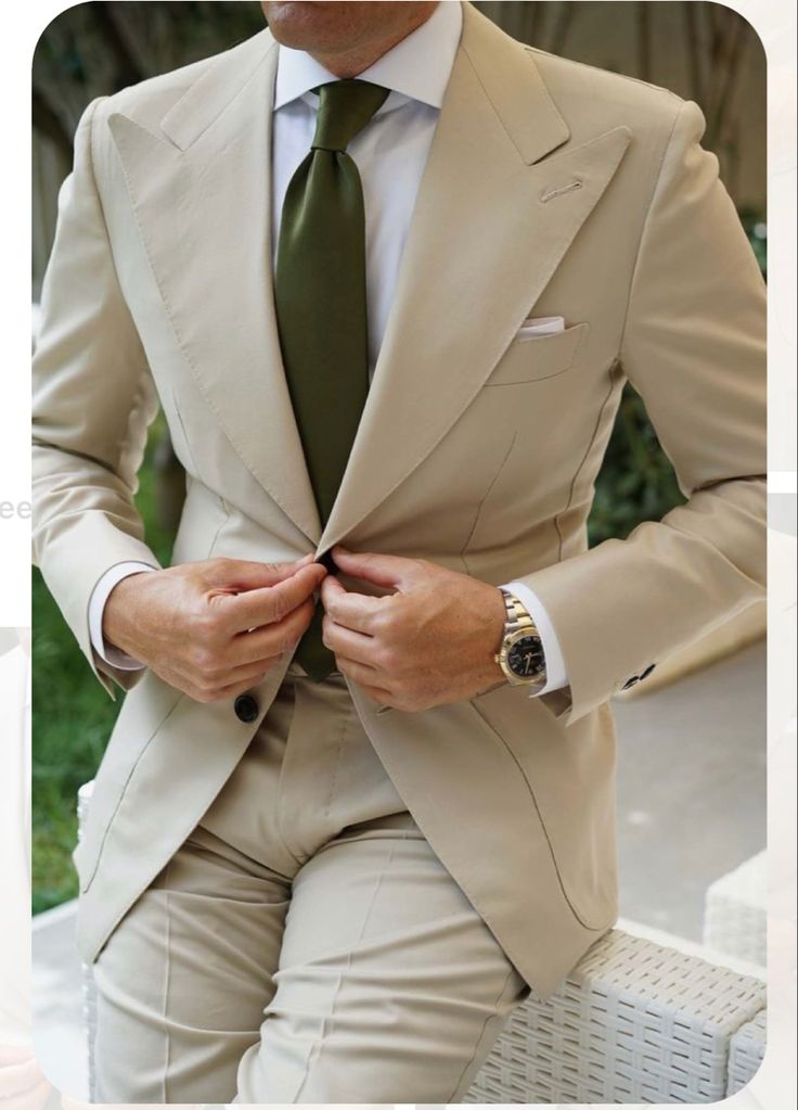 a man in a tan suit and green tie sitting on a white chair wearing a watch