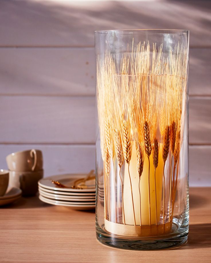 there is a glass with some wheat in it on the table next to plates and cups