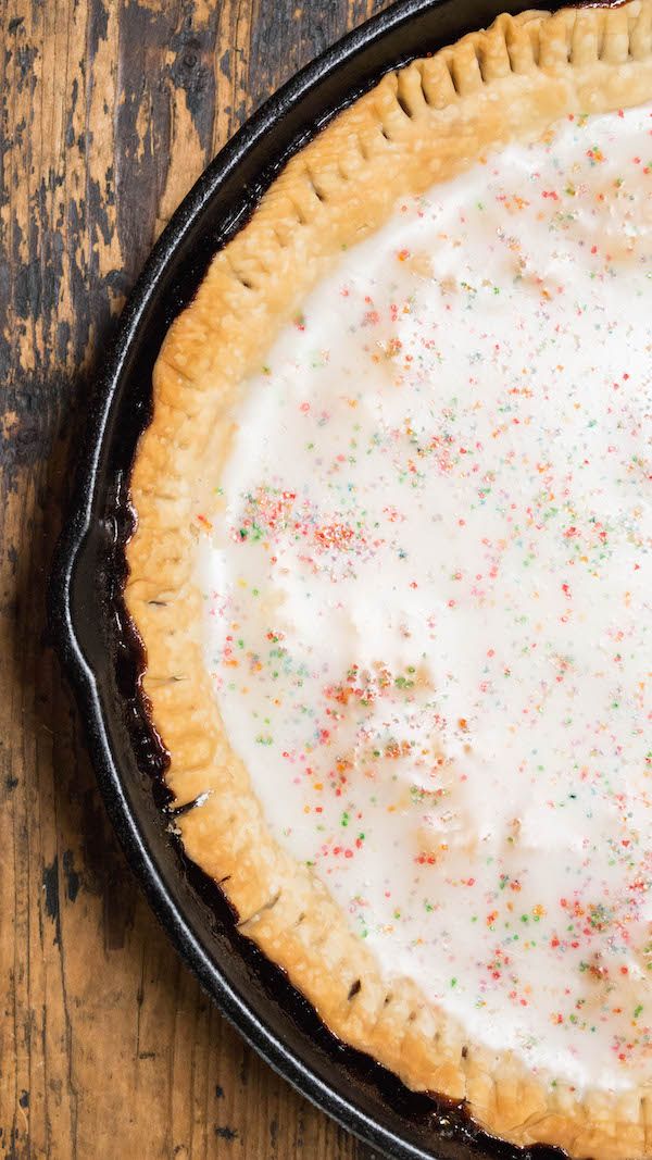 a pie with white frosting and sprinkles sitting on top of a wooden table