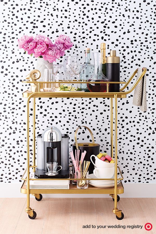 a gold bar cart with drinks on it and pink flowers in vases next to it