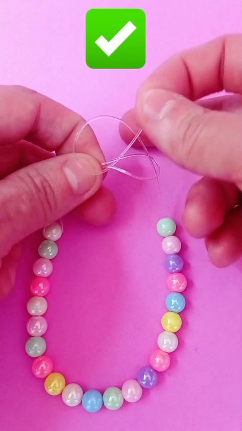 two hands are making a bead necklace with colored beads on a pink background and green check mark