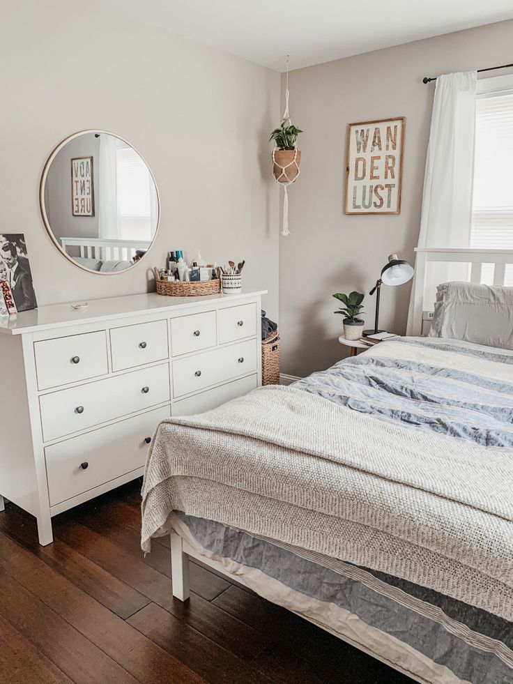 a bedroom with a bed, dresser and mirror next to a window in the room