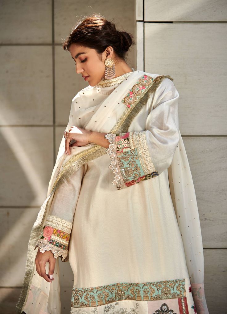 Editor's Note Featuring an ivory chanderi kurta enhanced with patchwork along the hemline. It is paired with ivory chanderi trousers and a georgette dupatta accentuated with mukesh, lace and patchwork border. Fabric: Chanderi: kurta & trousers, dupatta: georgette Color: Ivory Component: Kurta, trousers & dupatta Sleeve type: Full Neckline: Round Occasion: Festive Care: Dry Clean Only About the Designer Varun’s work marries the beauty of heritage Indian handcrafted embroideries with a modern colo Cream Cotton Silk Traditional Wear With Dupatta, Bollywood Style Tussar Silk Palazzo Set With Embroidered Border, Traditional Tussar Silk Palazzo Set With Embroidered Border, Tussar Silk Palazzo Set With Sheer Dupatta, Off White Anarkali Set With Embroidered Border, Cream Chanderi Palazzo Set With Resham Embroidery, Semi-stitched Cream Chanderi Palazzo Set, White Mulmul Salwar Kameez With Gota Work, Cream Bollywood Palazzo Set In Chanderi