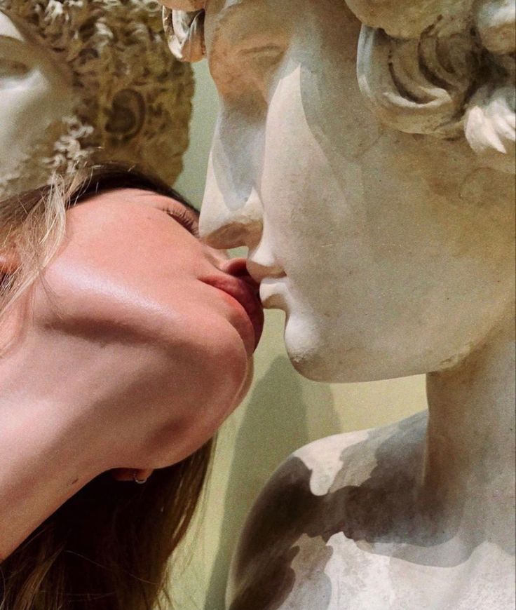 a woman is kissing the face of two statues