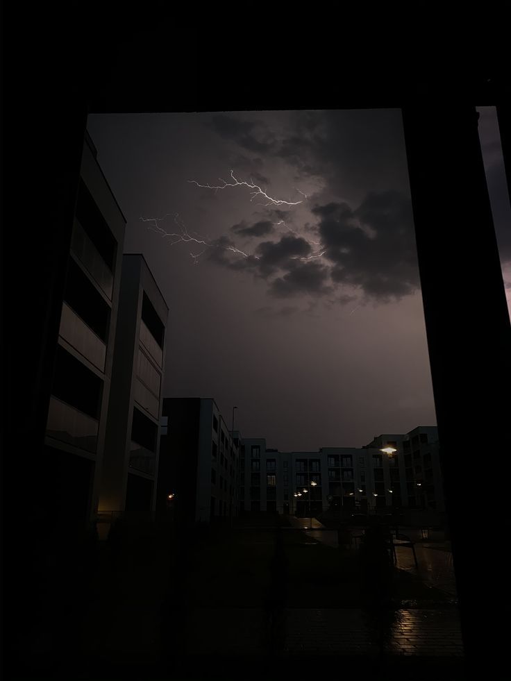 the sky is dark and cloudy at night with lightning in the distance over buildings on either side