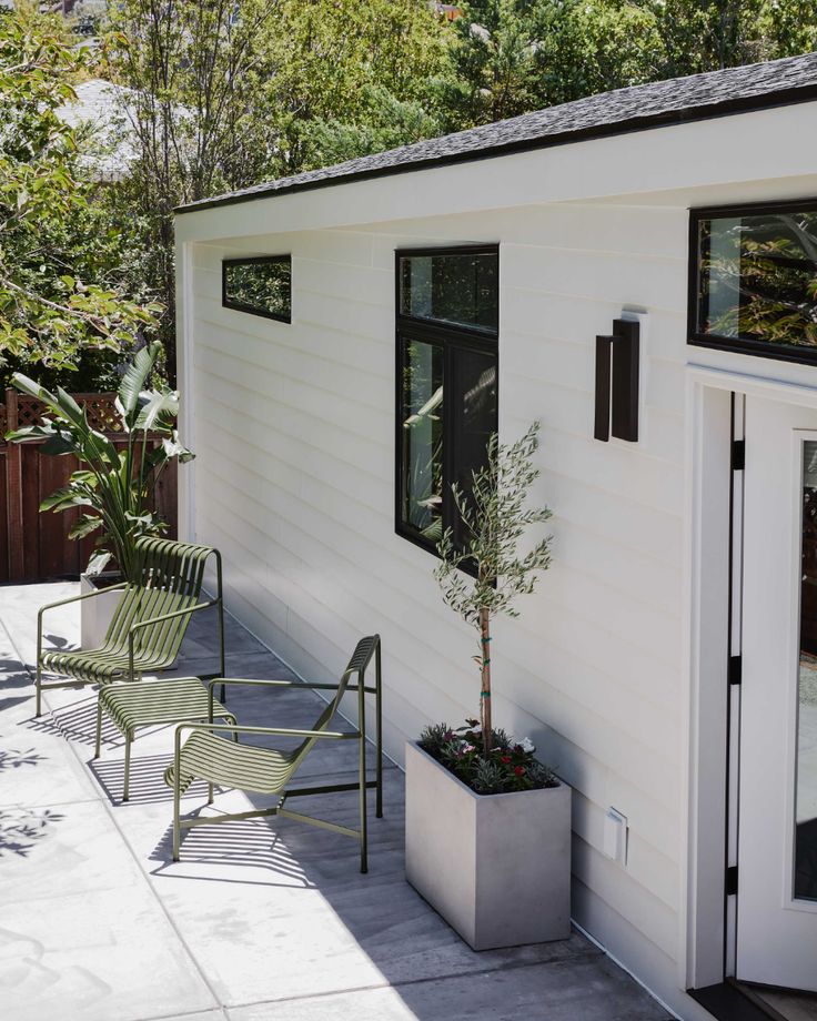 a small white house with two chairs and a potted tree