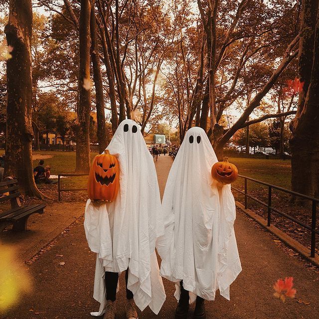 two people dressed up as ghostes standing in the middle of a park with trees