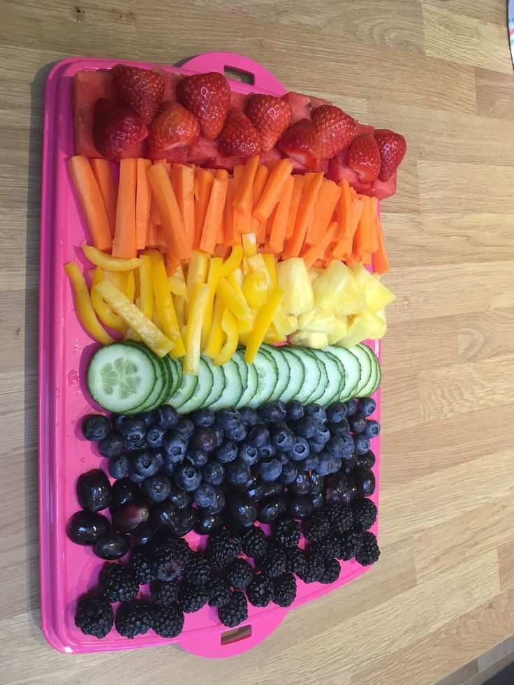 a pink tray filled with fruit and veggies on top of a wooden table