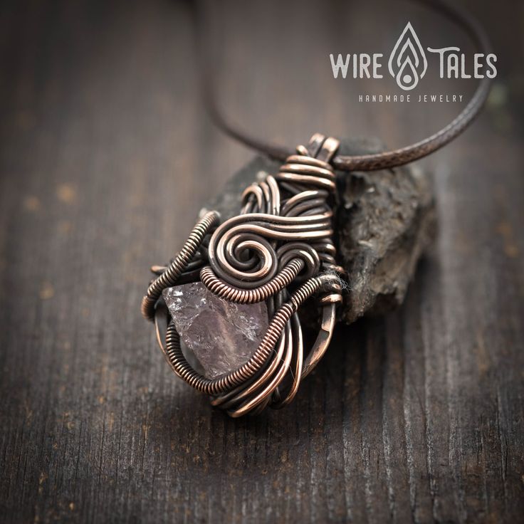 a wire wrapped pendant with a stone on a wooden table next to a piece of wood