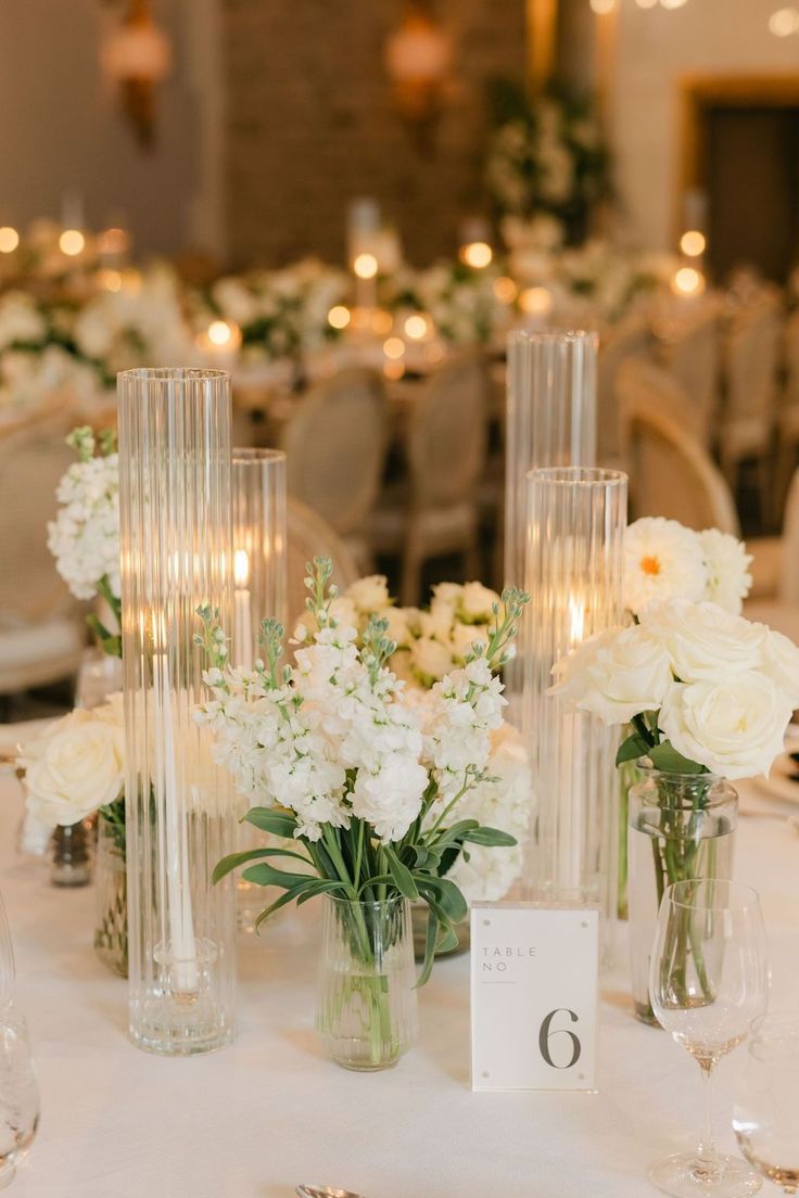 white flowers in vases on a table with candles and place cards for guests to sit at