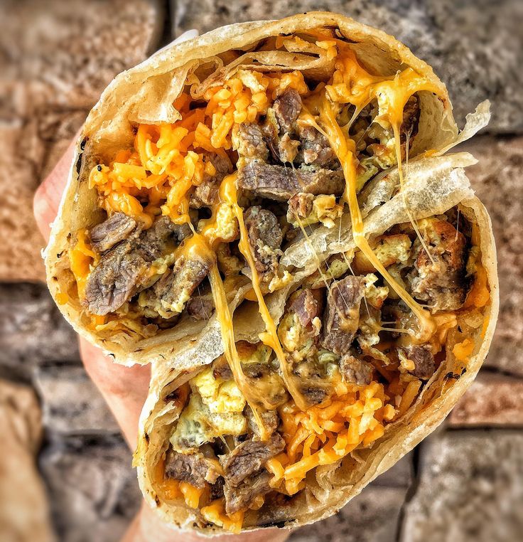 a burrito filled with meat and cheese sitting on top of a brick wall next to a person's hand