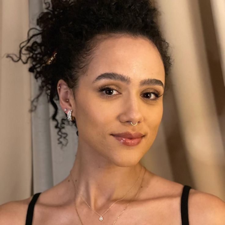 a woman with curly hair wearing a black tank top and silver earrings, looking at the camera