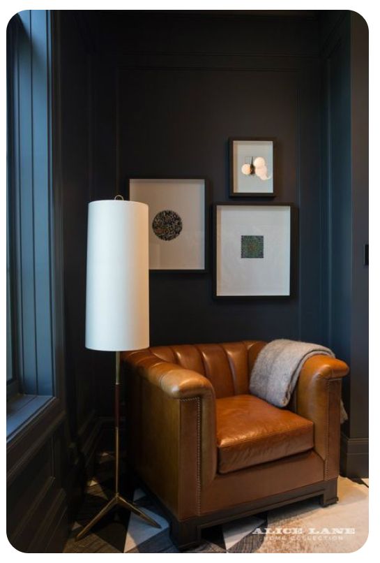 a brown leather chair sitting in front of a window next to a lamp and pictures on the wall