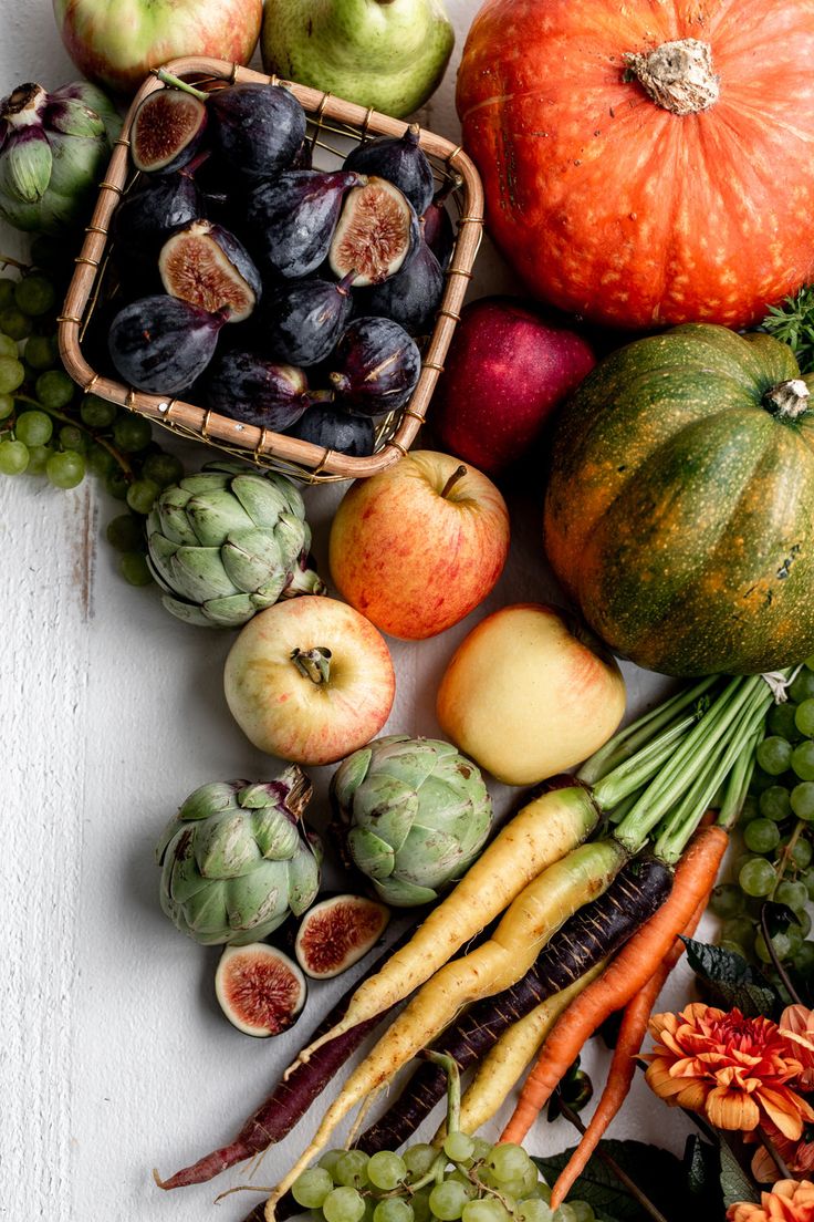 an assortment of fruits and vegetables on a white surface with pumpkins, apples, grapes, squash, artichokes, as well as well