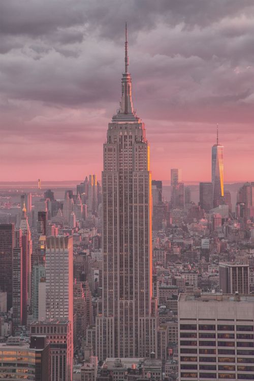 the empire building in new york city is lit up at sunset with clouds above it