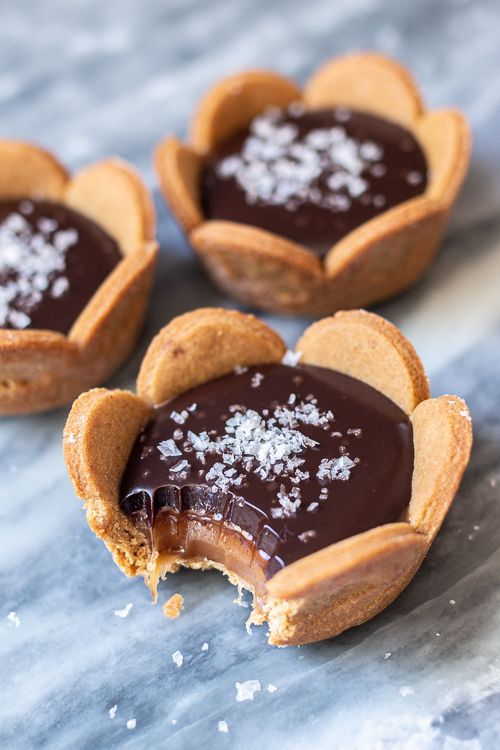 three chocolate tarts with sea salt in the middle on a marble counter top, ready to be eaten