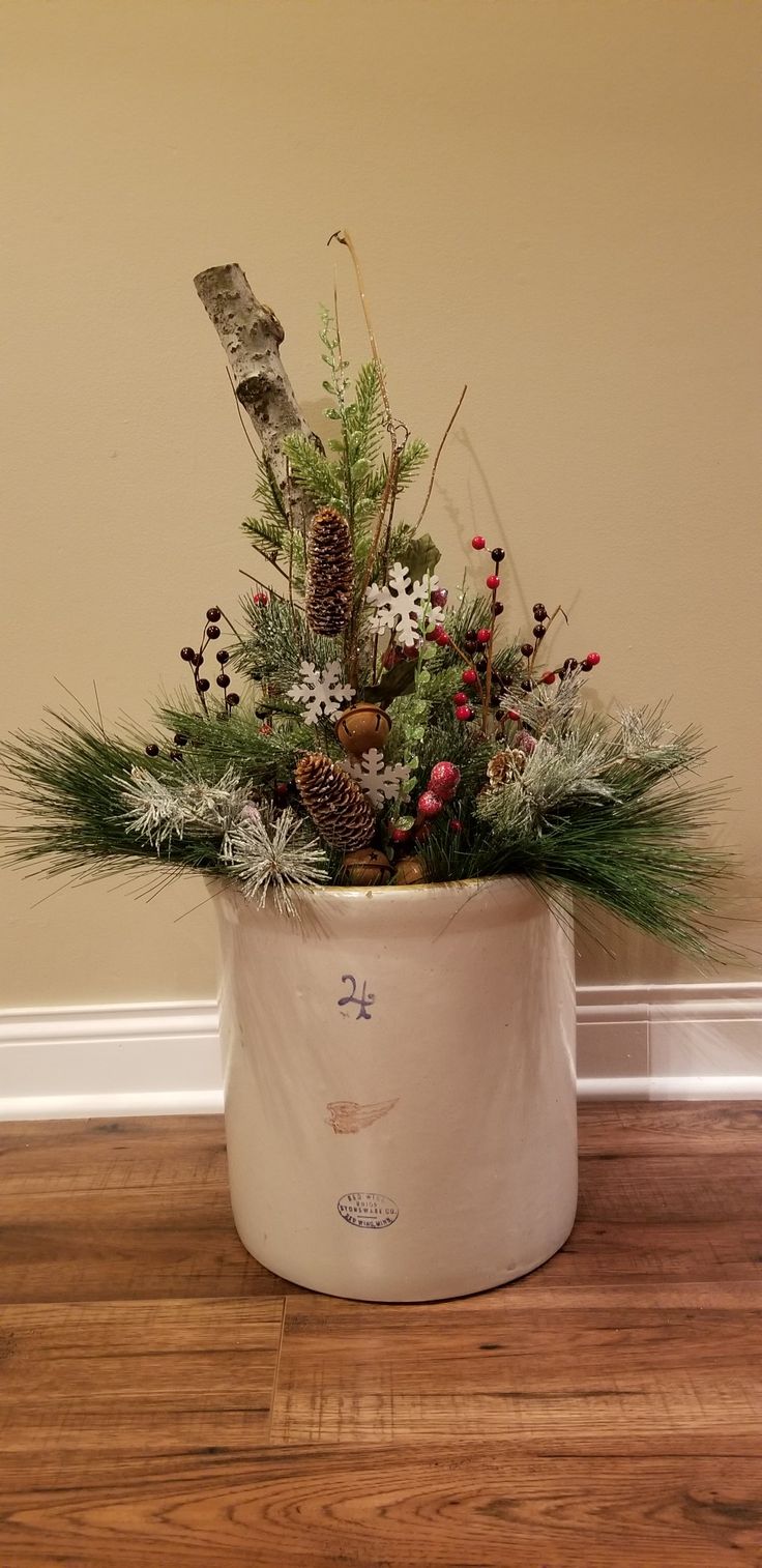 a potted plant with pine cones, berries and other greenery in it sitting on a wooden floor