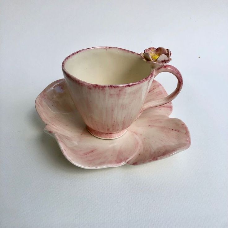 a pink cup and saucer with a flower on the side sitting on a white surface