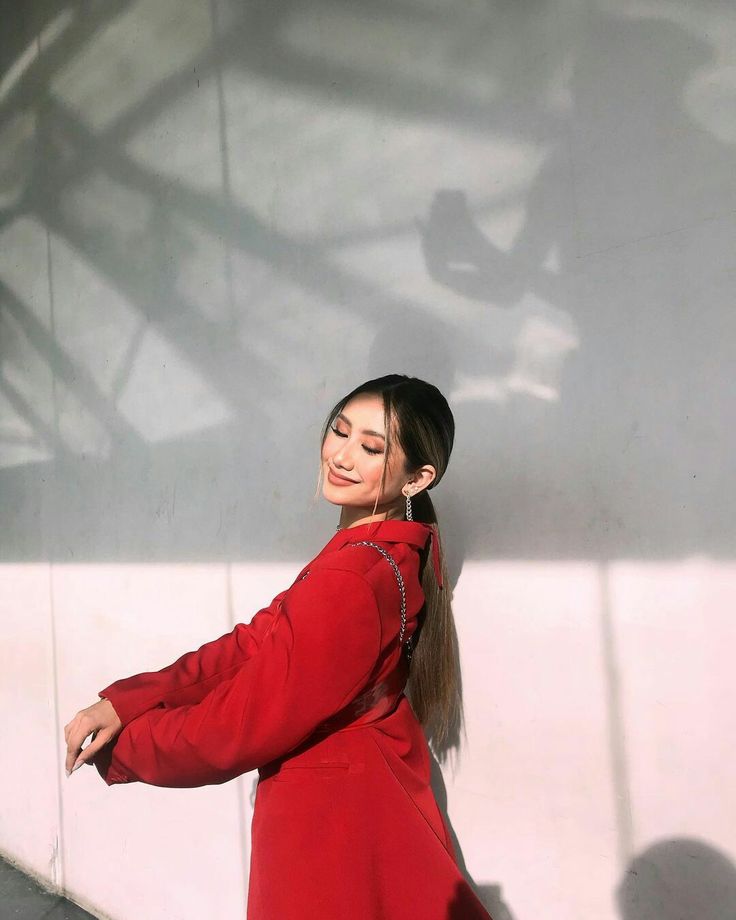 a woman in a red dress is leaning against a wall