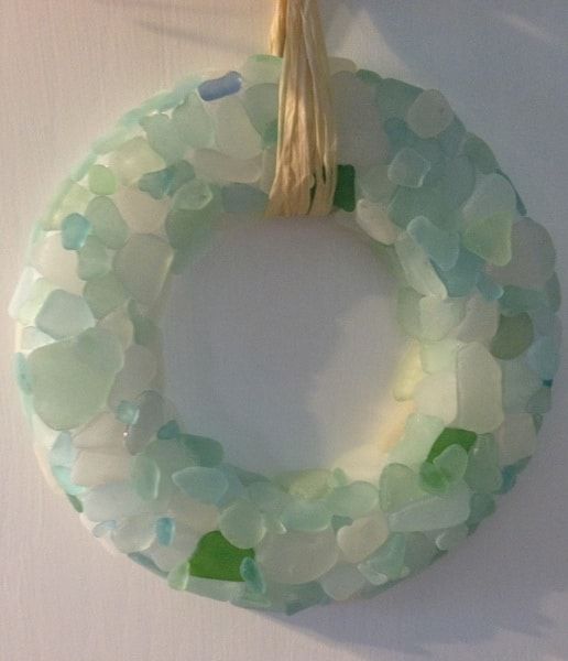 a wreath made out of sea glass hangs on the wall with a tassel hanging from it