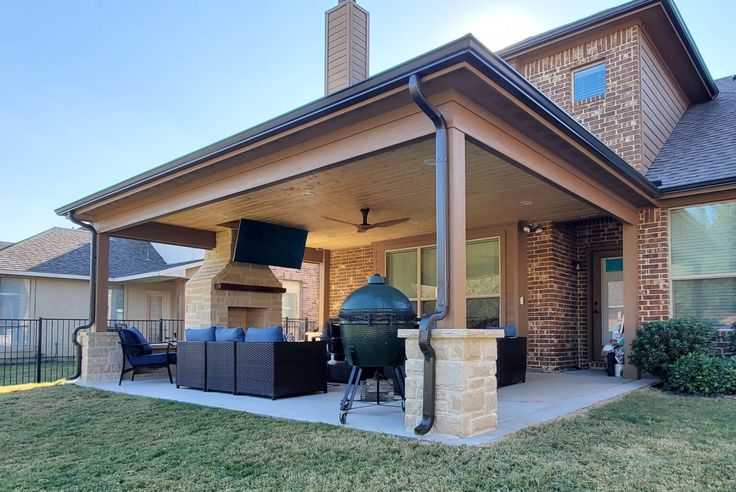 a covered patio with grill and outdoor furniture in front of the house on a sunny day