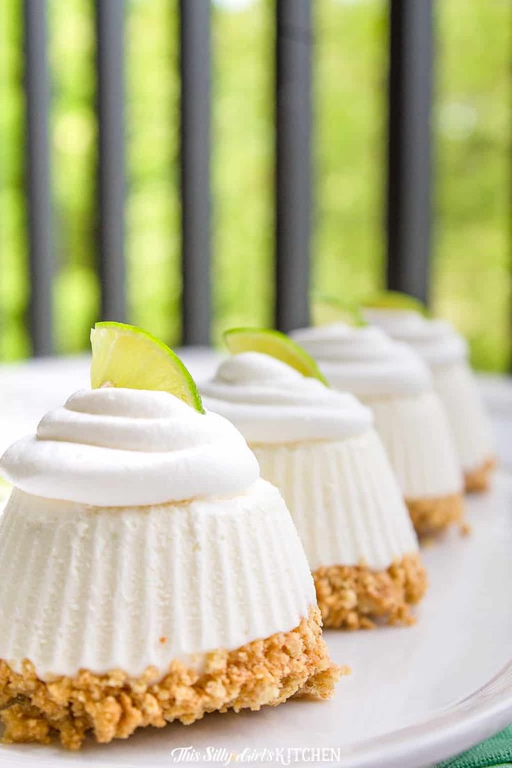 three small desserts on a white plate with lime wedges and whipped cream topping