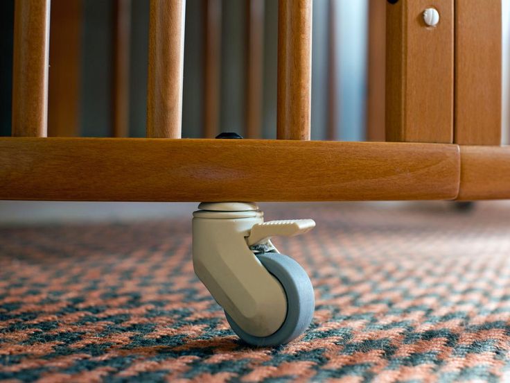 a close up of a wooden baby crib with wheels on the floor and carpet