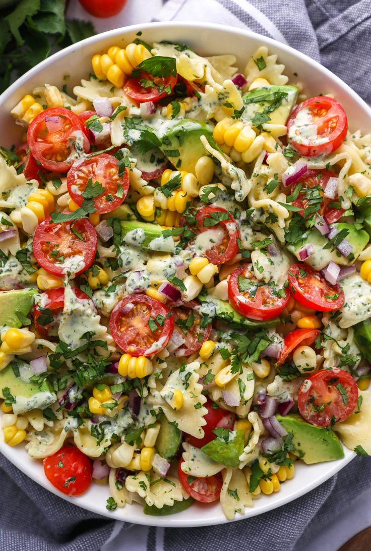 a large bowl filled with pasta salad and topped with tomatoes, corn, avocado, cilantro