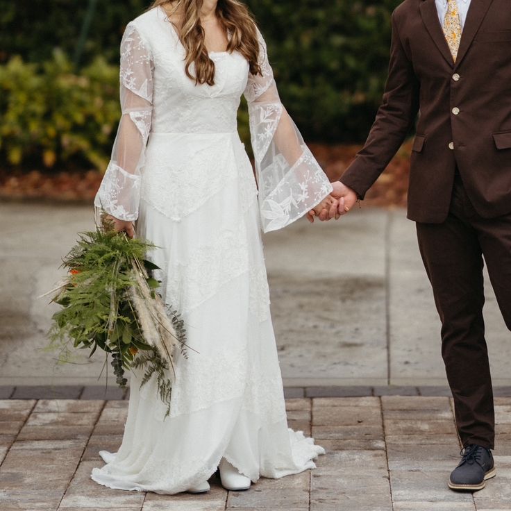 a bride and groom hold hands while walking down the street