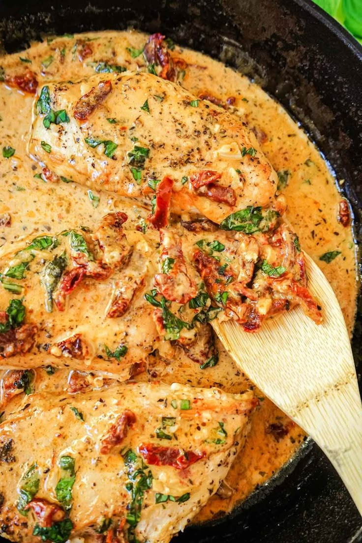 chicken with tomatoes and herbs in a skillet being stirred with a wooden spatula