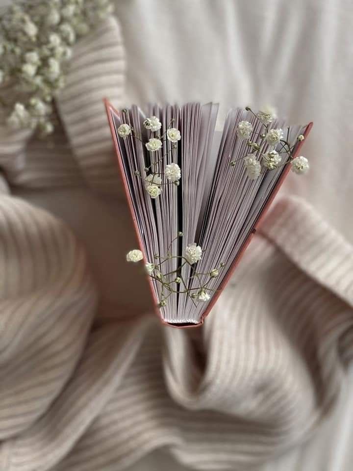 an open book sitting on top of a bed covered in white flowers next to a bouquet of baby's breath