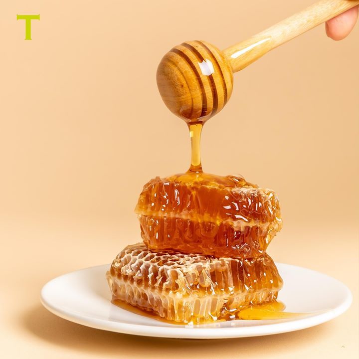 a wooden honey dipper on top of a piece of raw honey sitting on a white plate