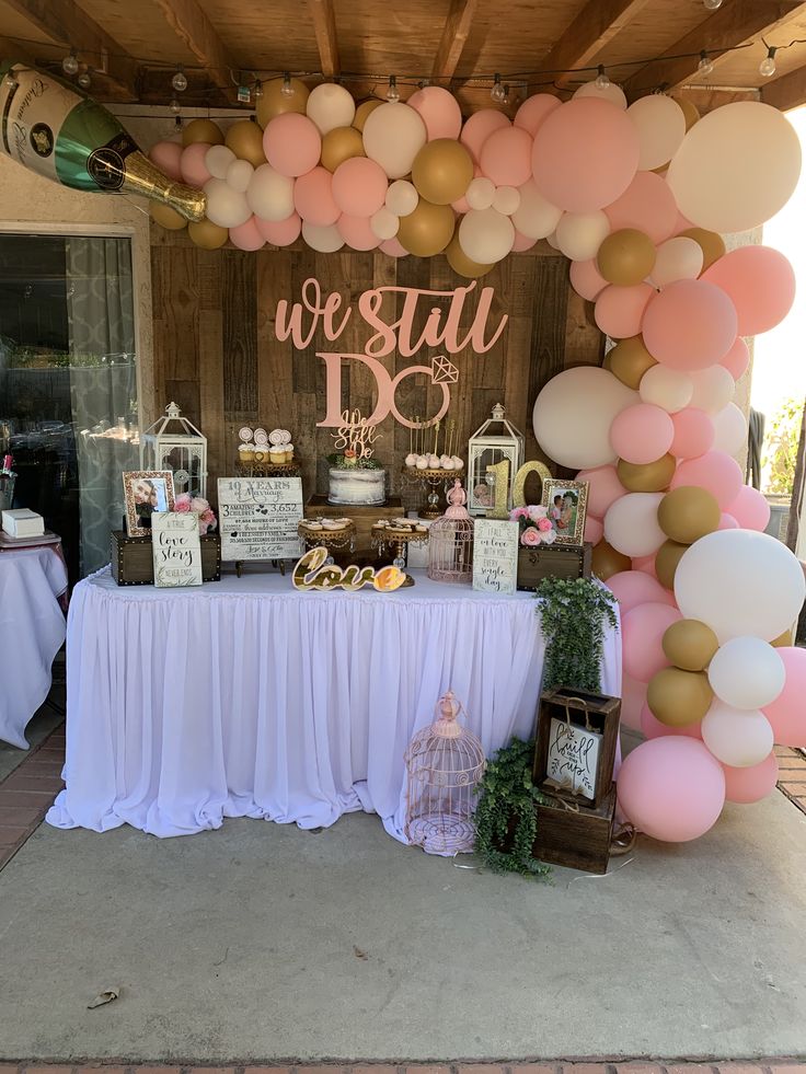 a table covered in balloons and desserts under a wooden structure with a sign that says we still do