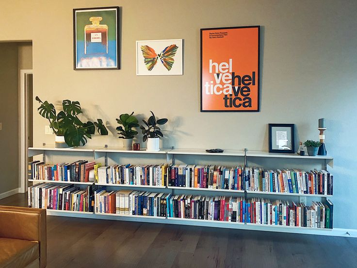 a living room filled with lots of books next to a wall covered in pictures and plants