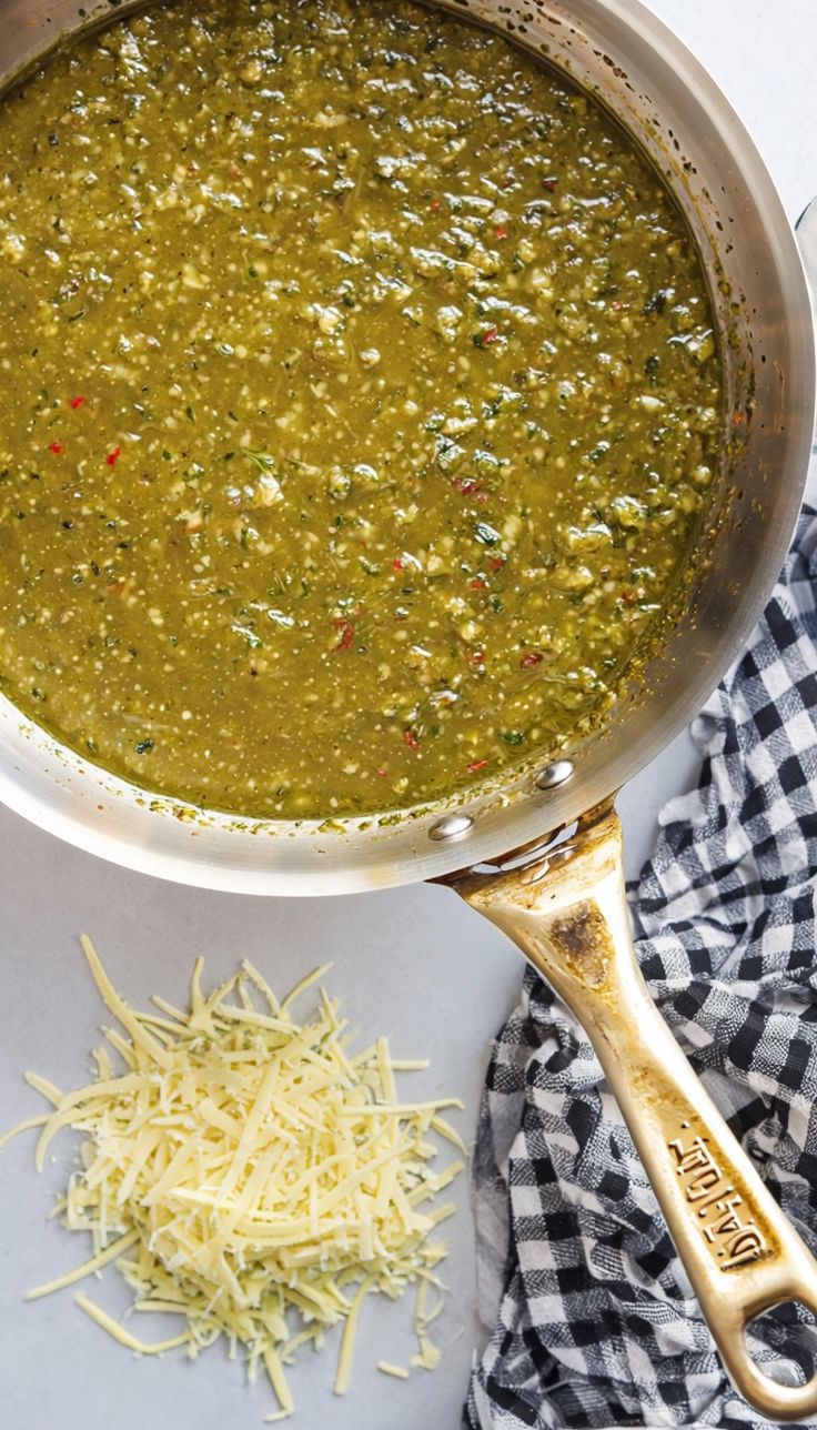 a large pot filled with green soup next to shredded cheese on a white counter top